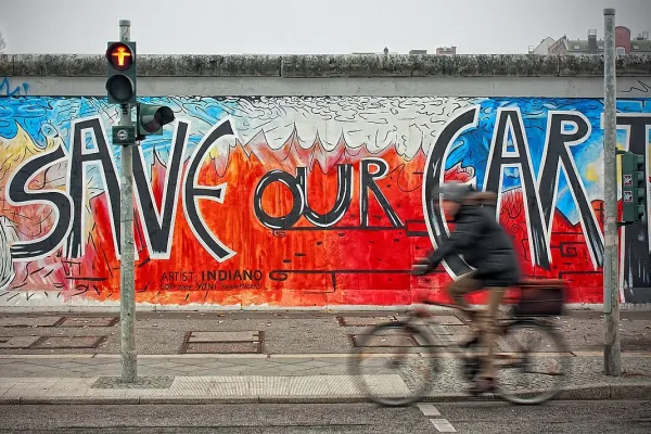 Blick auf die Graffiti-besprühte Berliner Mauer hinter einer roten Fußgängerampal: Save Our Earth